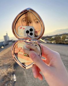 a woman taking a selfie with her cell phone in front of an open compact mirror