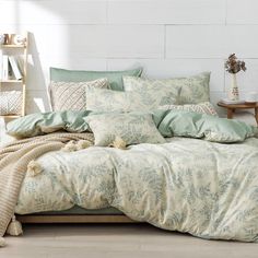 a bed with green and white comforters in a room next to a wooden table