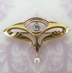 "An old mine cut diamond is centered on this antique Art Nouveau 14k yellow gold brooch. A white gold trim frames the .15 carat diamond, which has I grade clarity. A 3.3mm white pearl is suspended from a sophisticated hinged dangle. The brooch has  curvy flowing lines and shapes. The back is fitted with an old tube style hinge and hook closure. It is signed, \"E.K.\" and hallmarked, \"14k\" (gold). This brooch is in beautiful antique condition with minor wear. It would also look lovely as a pend Formal Art Nouveau Diamond Jewelry, Victorian Gold Diamond Brooches, Antique Gold Diamond Brooches, Antique Gold Brooches With Diamond Accents, Elegant Gold Brooches With Rose Cut Diamonds, Art Nouveau Wedding Brooches Hallmarked, Victorian Yellow Gold Diamond Brooches, Elegant Gold Brooches With Diamond Accents, Elegant Yellow Gold Brooch With Rose Cut Diamonds