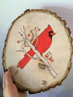 a hand holding a piece of wood with a red bird on it