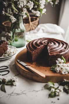 a chocolate cake sitting on top of a wooden cutting board next to a vase with flowers