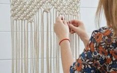 a woman is working on a wall hanging with beads and chains, in front of a white tiled wall