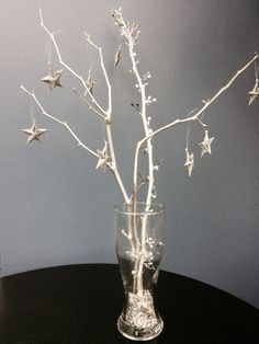 a glass vase filled with branches and stars on top of a black table next to a gray wall