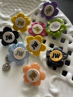 several different colored flower shaped buttons sitting on a white plate with the letters w and j