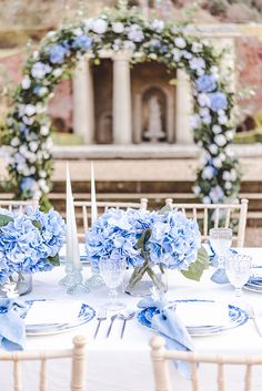 the table is set with blue flowers and white place settings for an outdoor wedding reception