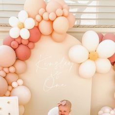 a baby is sitting in a high chair with balloons on the wall behind her and smiling at the camera