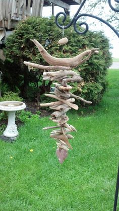 a wind chime made out of driftwood in the grass next to a birdbath