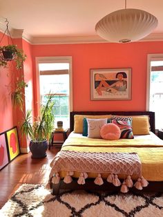 a bedroom with orange walls and wooden flooring is pictured in this image, there are potted plants on the far side of the bed