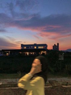 a woman walking down the street while talking on her cell phone at dusk with a house in the background