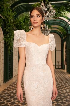 a woman in a white dress standing on a brick floor with greenery behind her