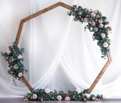 a wooden frame with flowers and greenery around it on a white cloth covered backdrop