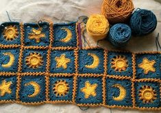 a crocheted blanket with sun, moon and stars on it next to balls of yarn