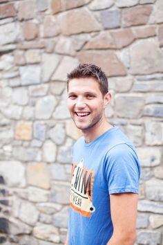 a man standing in front of a stone wall with his hand on his hip and smiling at the camera