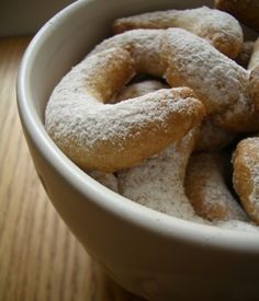 a white bowl filled with powdered sugar covered donuts on top of a wooden table