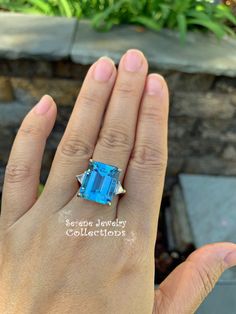 a woman's hand holding a blue ring with an emerald center stone in the middle