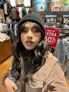 a woman with long hair wearing a black hat and jacket in a clothing store looking at the camera