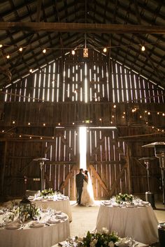 a bride and groom standing in front of a barn door with their wedding party tables