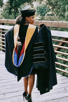 a woman walking across a wooden bridge wearing a graduation gown and cap with a tassel