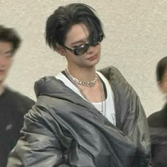 a man with black hair wearing sunglasses and a leather jacket walking past other people in front of a white wall