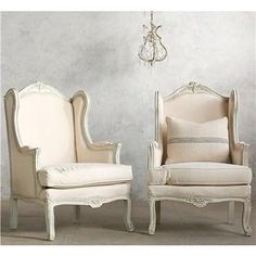 two white chairs sitting next to each other in front of a wall with a chandelier