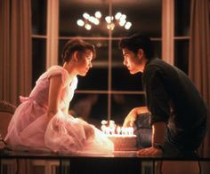 a man and woman sitting at a table in front of a cake with lit candles