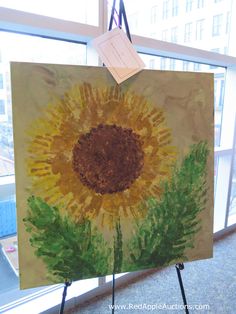 an easel holding up a painting of a sunflower in front of a window