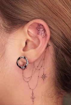 a woman's ear with tattoos on it and a chain behind the ear that has a flower