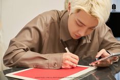 a man sitting at a table writing on a piece of paper with a pen in his hand