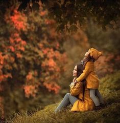 two people sitting on the ground in front of trees with fall foliages behind them