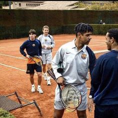 four men standing on a tennis court holding racquets and talking to each other