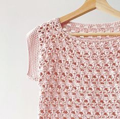 a pink crocheted shirt hanging on a wooden hanger next to a white wall