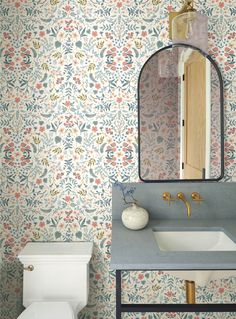 a bathroom with floral wallpaper and a mirror above the sink, along with a toilet