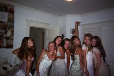 a group of young women standing next to each other in a living room with white walls