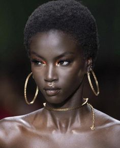 a model with dark skin and gold jewelry on her face, wearing large hoop earrings