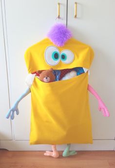 a stuffed toy in a yellow bag with eyes and arms, holding a teddy bear