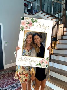 two women standing next to each other in front of stairs holding up a photo frame