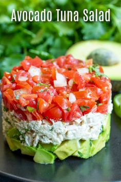 an avocado tuna salad on a black plate with lettuce and tomatoes