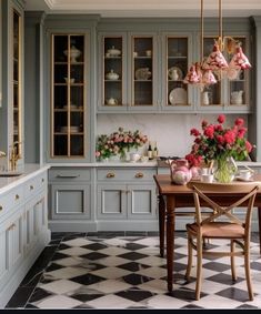 a kitchen with checkered flooring and cabinets in grey colors, including pink flowers on the table