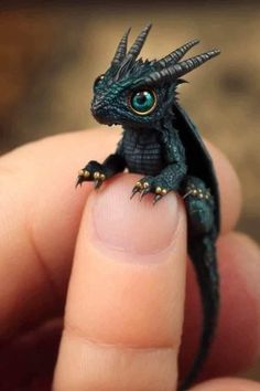 a tiny black lizard sitting on top of someone's finger with its eyes wide open