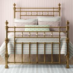 a gold metal bed frame with pillows and blankets in a pink walled room, against a striped wall