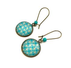 two earrings with blue and white designs are hanging from metal hooks on a white surface