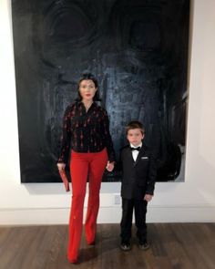 a woman standing next to a young boy in front of a black and white painting