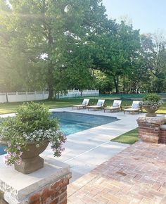 an empty swimming pool surrounded by lawn chairs and flowers in the foreground, next to a brick fire hydrant