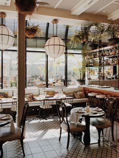 the inside of a restaurant with tables, chairs and plants on the windowsills