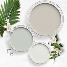 three different shades of gray paint with white flowers and palm leaves on a light grey background