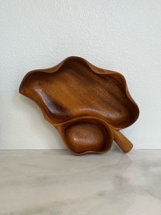 a wooden bowl sitting on top of a counter next to a white wall with two spoons in it