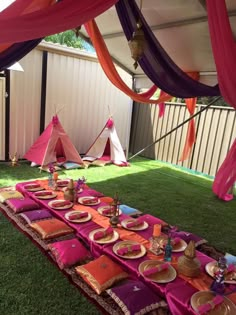 a table set up for a party with plates and napkins on it in the grass