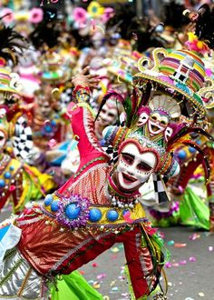 people dressed in colorful costumes and masks are dancing on the street with confetti all around them