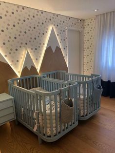 two baby cribs in the middle of a room with mountains on the wall