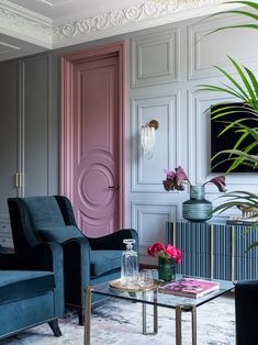 a living room with two blue chairs and a pink door in the corner, next to a coffee table